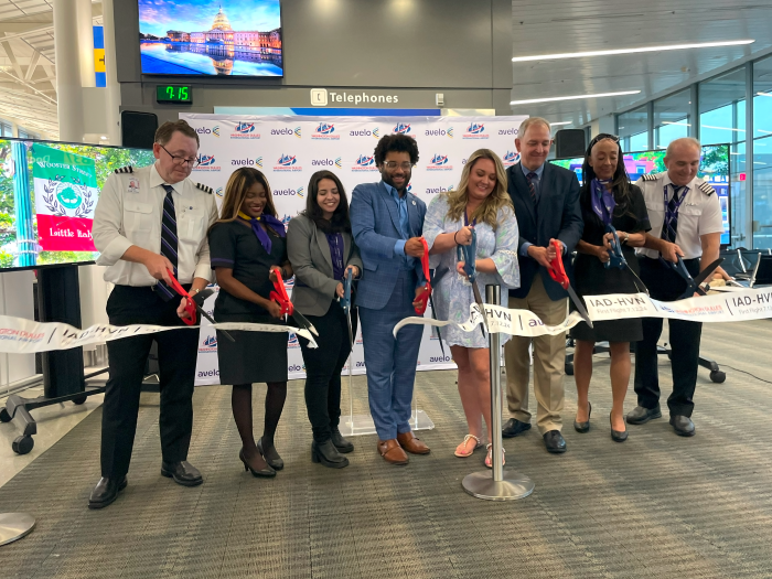 Eight people cut a ceremonial ribbon inside an airport for an airline launch.